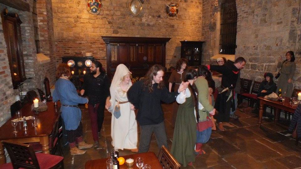 People doing a line dance in a hall with Medieval architecture