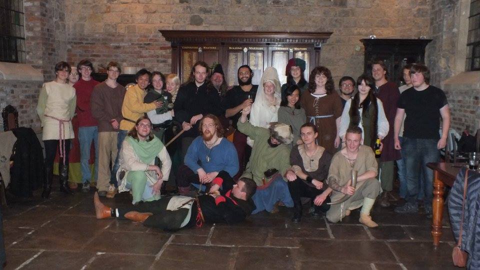 Group picture of people in Medieval and early Renaissance garb in a hall with Medieval architecture
