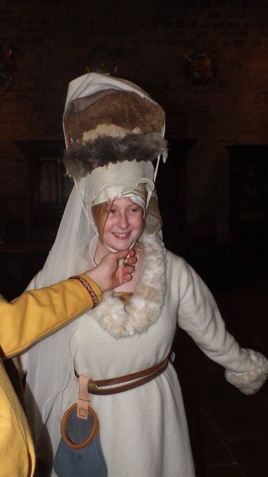 A woman in Medieval dress, several furry hats stacked on top of her head